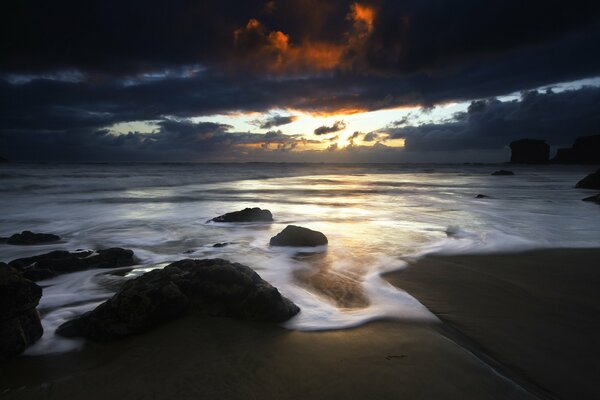 Sunset on the shore with rocks and clouds