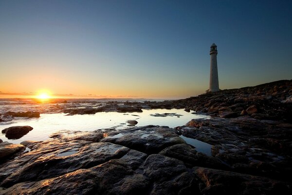 Lighthouse at sunrise. Rocky shore by the sea