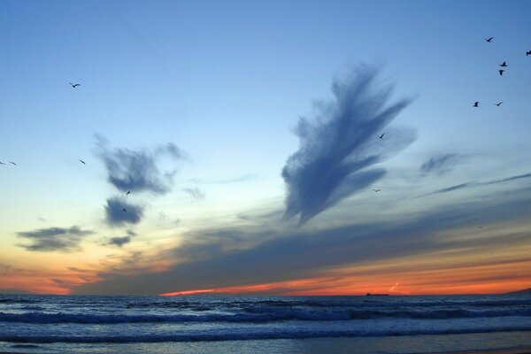 The sea waves over the horizon, colliding with clouds in the sky