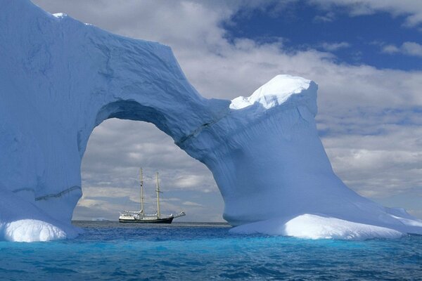 A white sailboat on the waves behind an iceberg