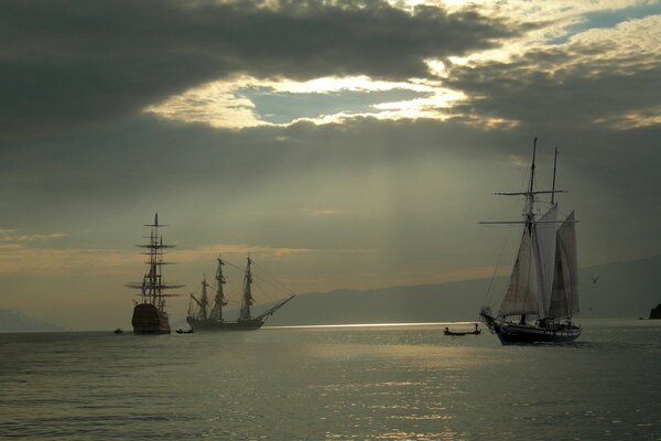 Sailboats and a yacht at sea. Sunlight through clouds