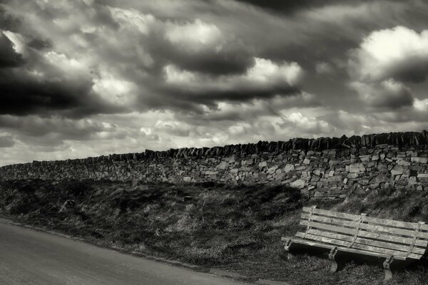 Banco junto a la carretera y la pared de ladrillo. Foto en blanco y negro