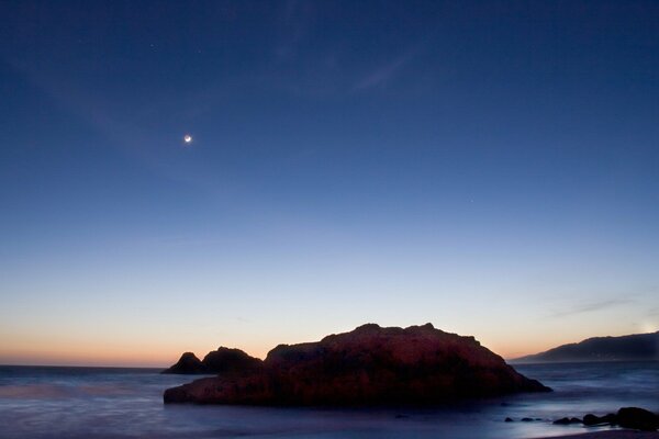 Roca en el mar al atardecer a la luz de la Luna