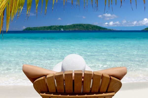 A girl in a hat is lying on a wooden sunbed on the seashore