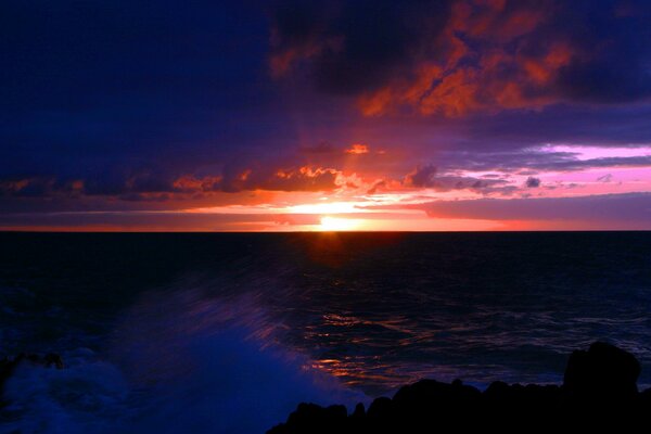 La vague se brise sur le rivage au coucher du soleil