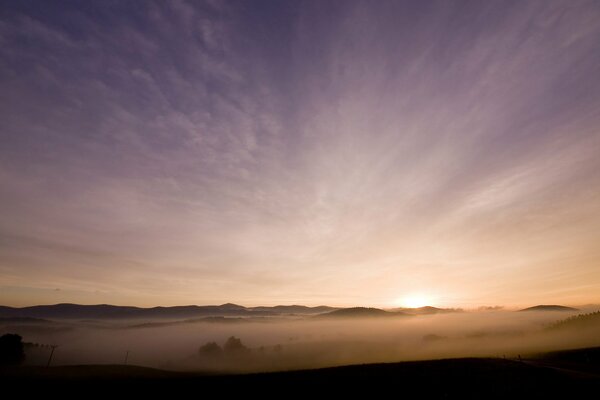 Morning fog. The sun rises behind the hills