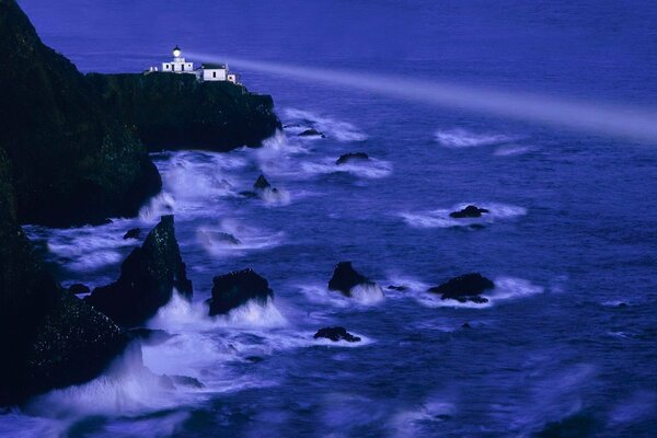 The beam from the lighthouse on the background of waves hitting the rocks