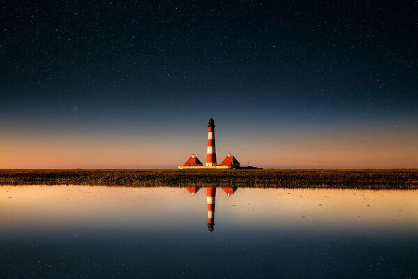 A lighthouse in the distance is reflected in the water