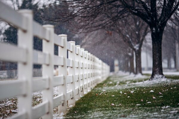 A city street with a white fence and the first snow