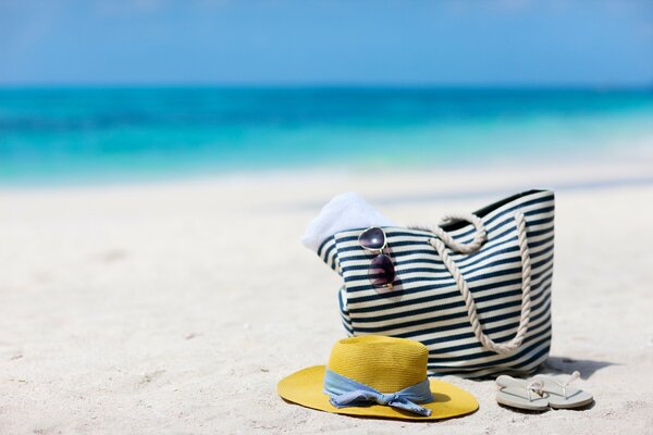 Tasche und Hut am Sandufer des blauen Meeres