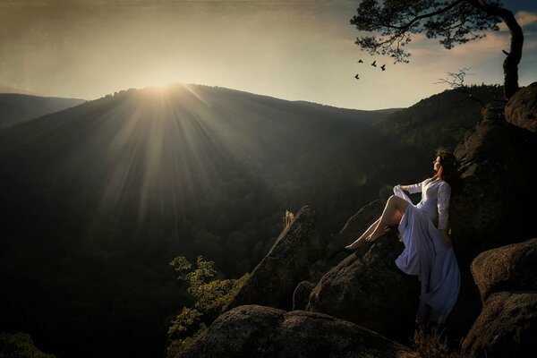 A girl on the rocks in the mountains against the background of the setting sun