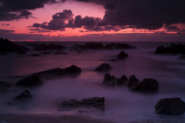 Puesta de sol rosa en la niebla del mar entre las rocas