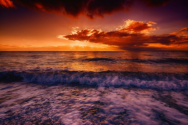 Brandung vor dem Hintergrund des Glühen im Meer mit Wolken