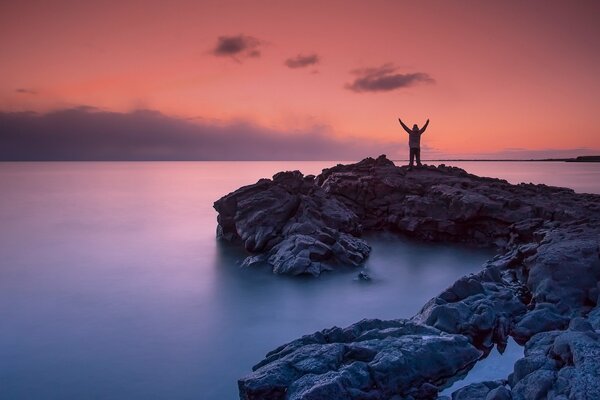 A man on a rocky seashore at sunset