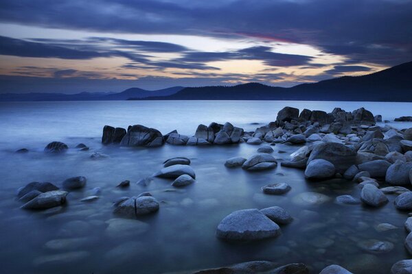 Piedras en la orilla del mar contra las montañas y las nubes