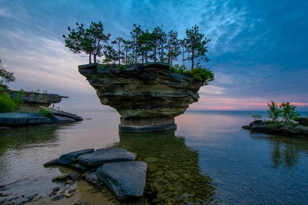 There is a rock in the sea at sunset