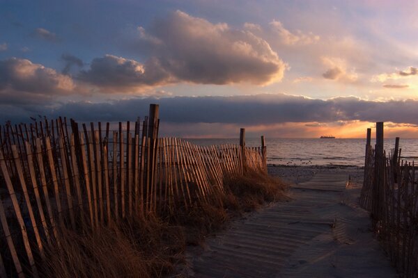 Der Weg zum Strand zwischen den Zäunen im Sonnenuntergang