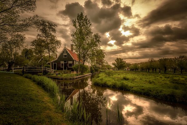 A house with a lake and greenery under twilight clouds