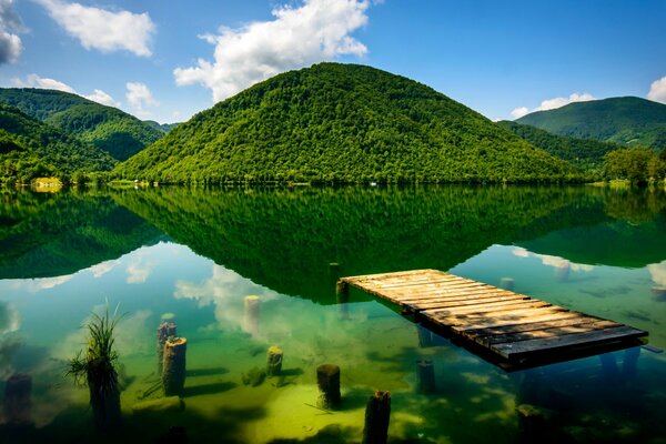 A green place with a pier, mountains, a river