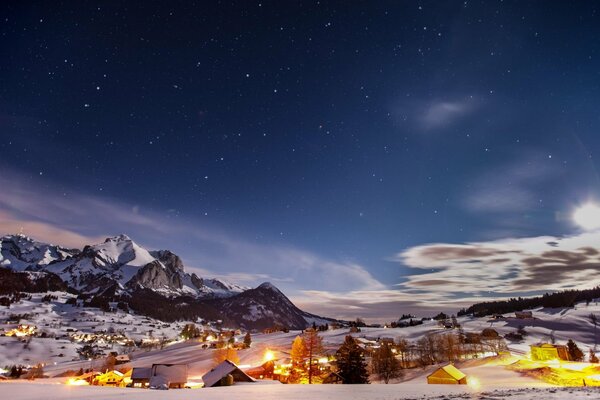 Lichter in Häusern und Füßen der Berge unter dem Sternenhimmel im Winter