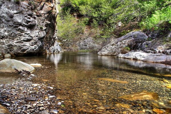 The purest water with pebbles on the background of high rocks