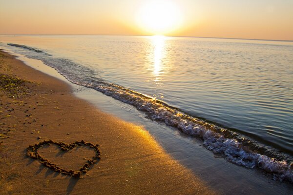 Herz auf dem Sand vor dem Hintergrund des Sonnenuntergangs am Meer