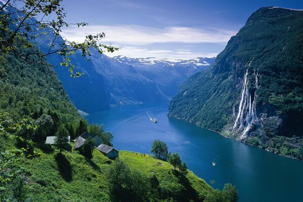 Un río de montaña en Noruega de belleza indescriptible con pequeñas casas en campos verdes y con cascadas que desembocan en el río