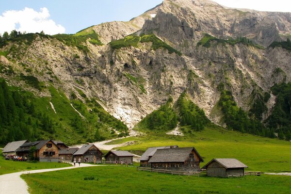 A mountainous area with small wooden houses greenery and a road on a sunny summer day