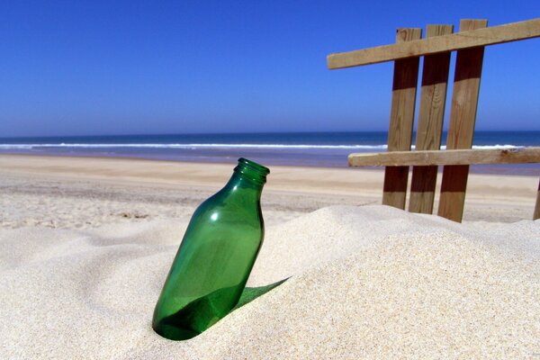 Une bouteille vide coincée dans le sable au bord de la mer