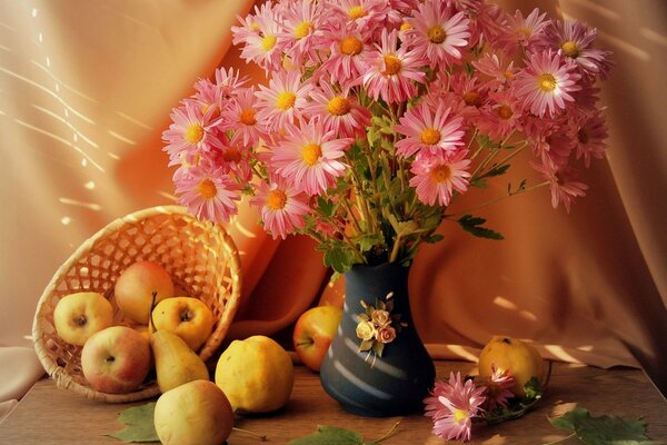 Flowers are in a vase and next to a basket of apples