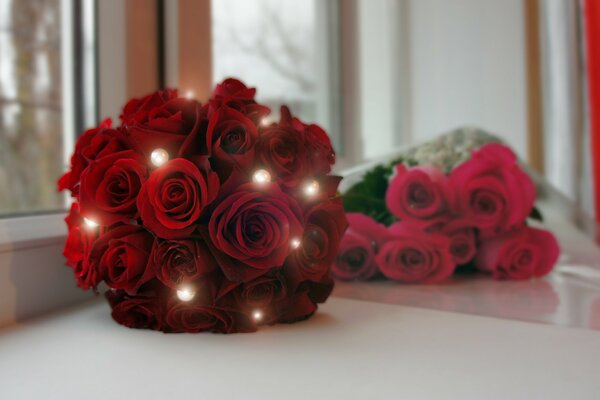 Ein Strauß scharlachroter Rosen und ein Strauß roter Rosen liegen auf der Fensterbank