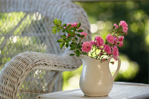 Różowe kwiaty w dzbanku na stole przy krześle