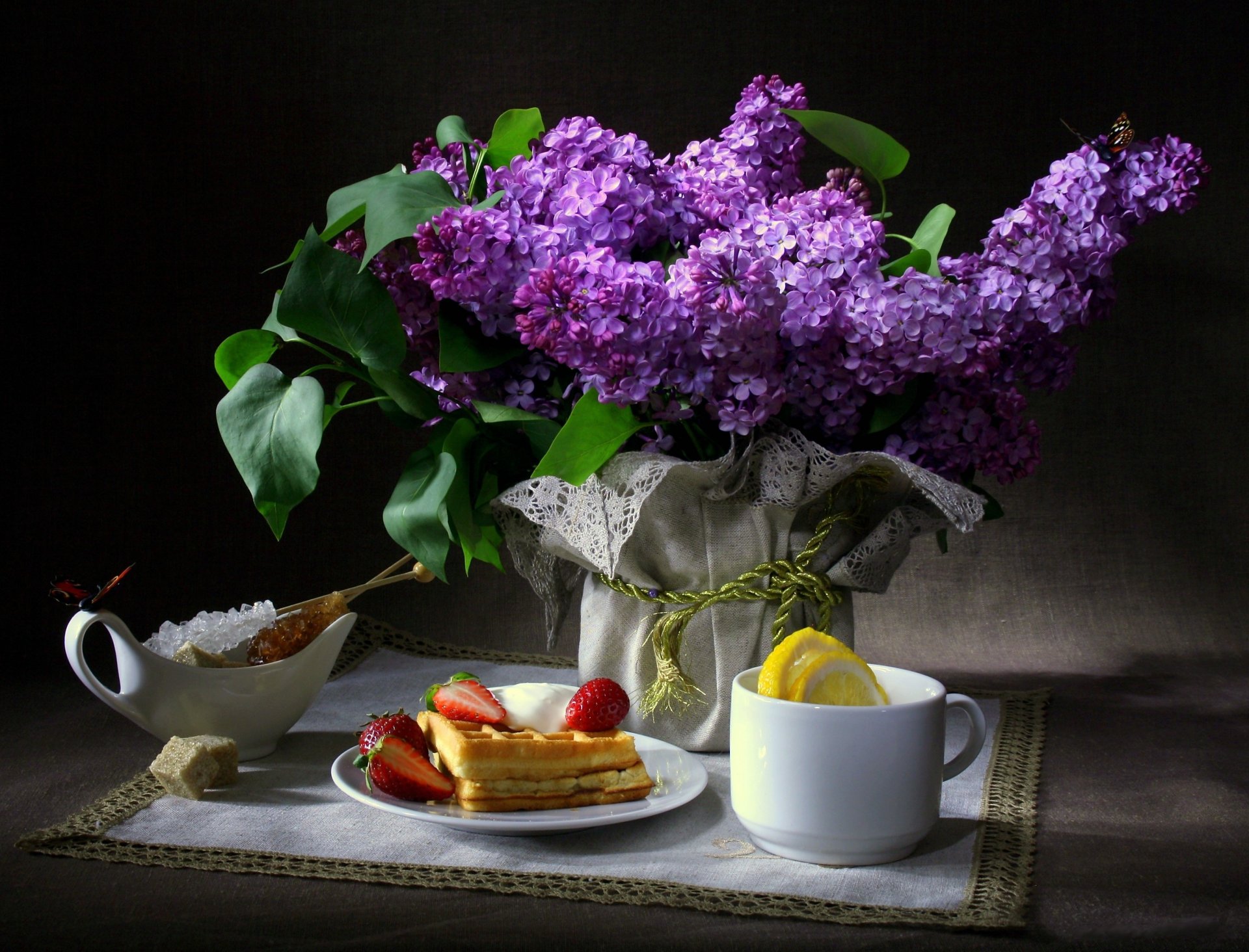 naturaleza muerta flores lila mariposas desayuno gofres fresa taza limón azúcar servilleta fondo oscuro