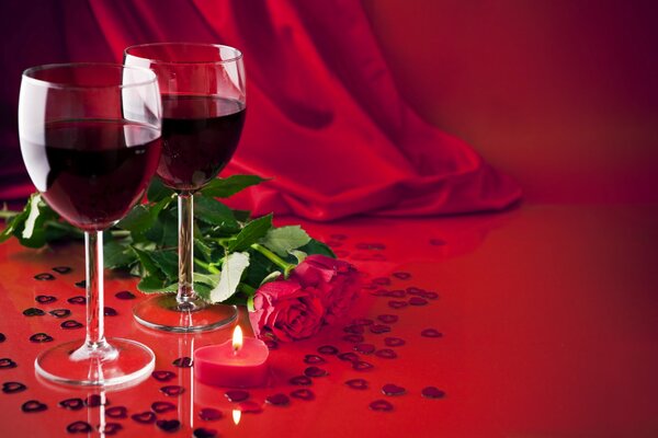 Dos copas de vino tinto y dos rosas sobre fondo rojo