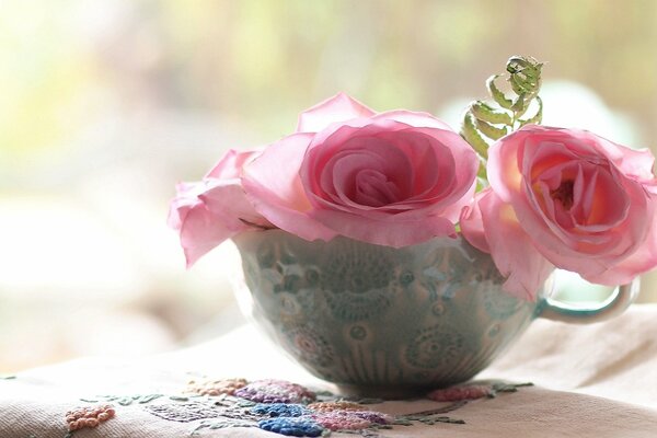 Una taza de rosas cerca de una servilleta bordada
