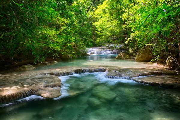 A river in Thailand among foliage with a small waterfall