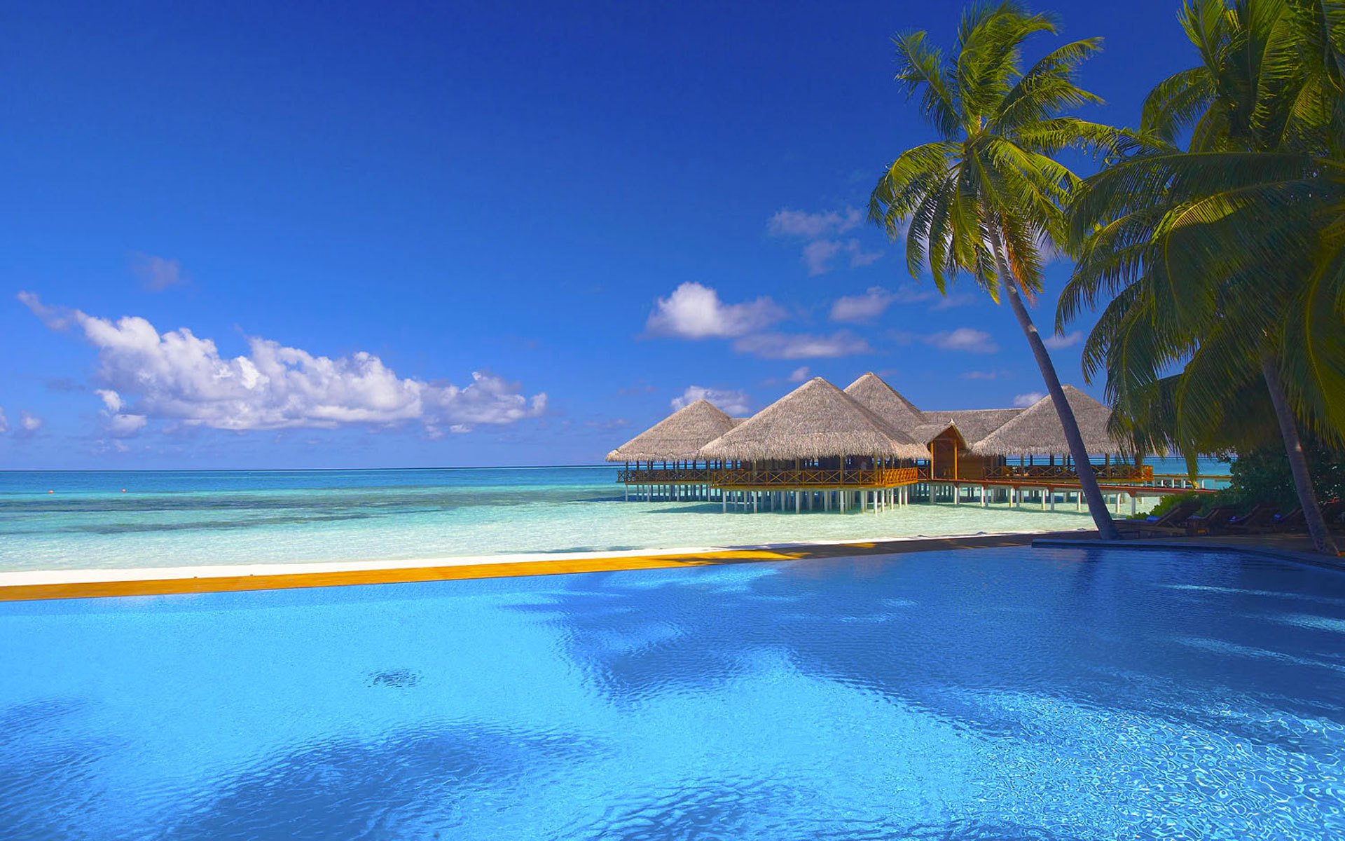 mare oceano spiaggia cabine palma palme piscina lettini cielo nuvole sabbia