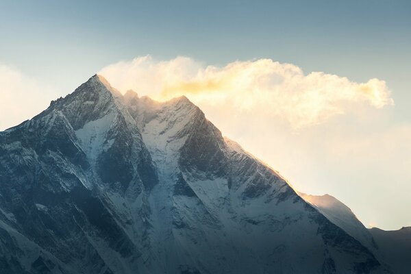 Snowy mountain top on the background of the sky with clouds