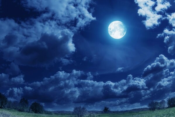 Full moon in the sky with clouds over a green field