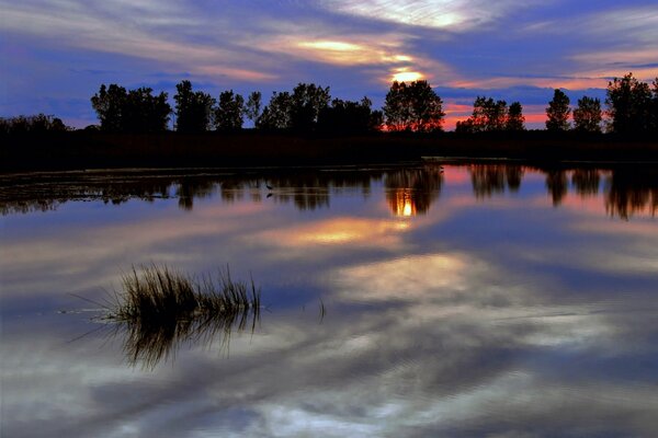 Die ruhige Oberfläche des Abendflusses reflektiert den Himmel