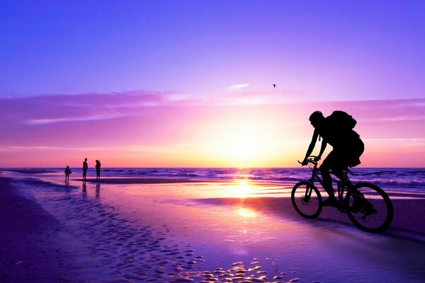 A man rides a bicycle along the beach at sunset