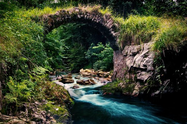 Ponte semicircolare in pietra su un fiume roccioso tempestoso