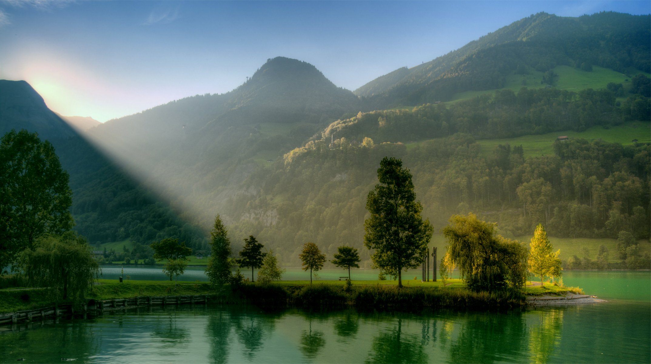 mountain hills tree green river blue cloudless sky sun sunrise light rays landscape