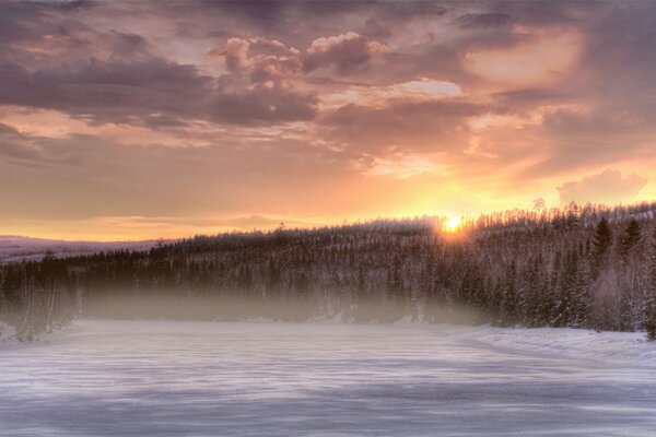 Sonnenuntergang und ein gefrorener Fluss, der mit Nebel bedeckt ist