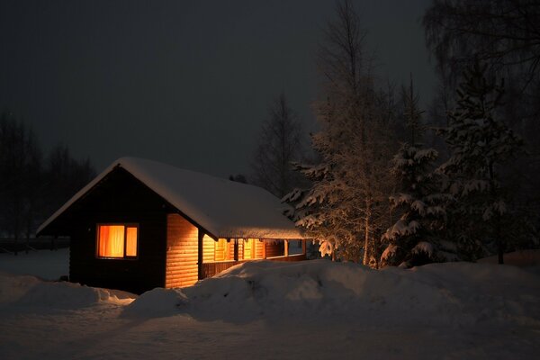 Warm light in winter breaking out of the house into the snow in the evening