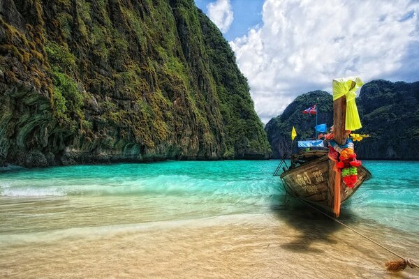 A small brightly decorated ship entered the sea bay with azure waters and green rocks