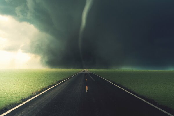 There is a black tornado in the green fields on the road