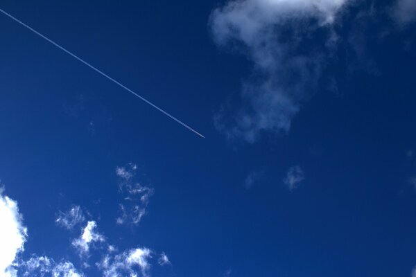 The trace of the plane in the blue sky among the clouds