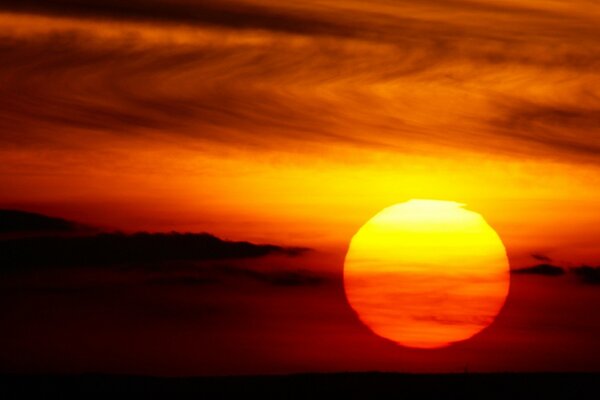 Imagen de una puesta de sol con un enorme sol naranja y niebla