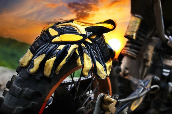 Gelbe Motorradhandschuhe auf einem Motorrad vor dem Hintergrund der untergehenden Sonne